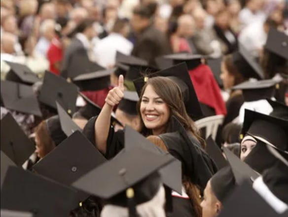 A young woman smiling and holding her thumbs up in between other bachelor students